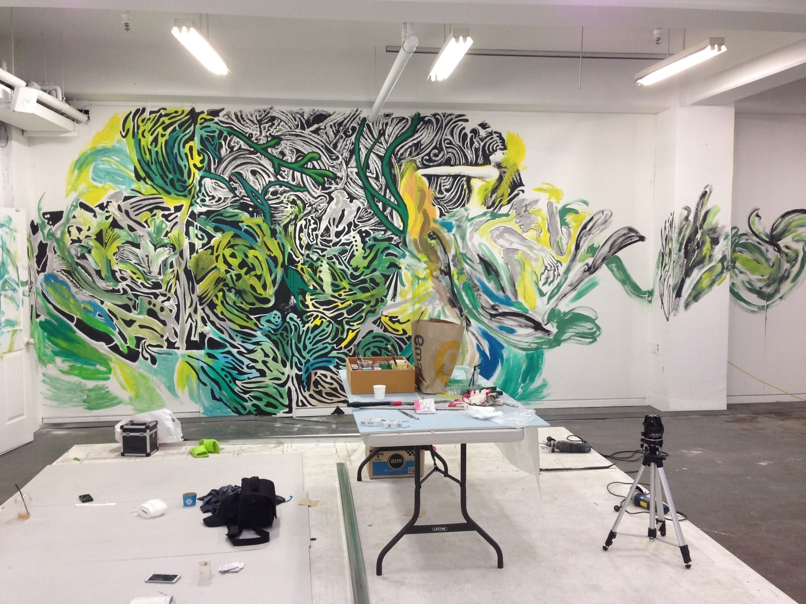 Green and yellow mural in progress beside a work table