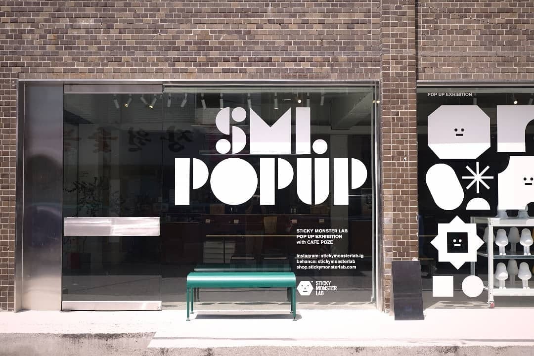 SML POPUP 글자와 캐릭터 그래픽을 붙인 카페 포제 유리창과 그 앞의 초록색 벤치